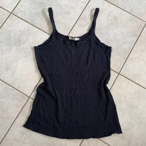 Svart prickig linnetopp från Saint Tropez - Säljer en söt marinblå linnetopp från Saint Tropez med små vita prickar. Toppen har smala axelband och en liten dekorativ blomma framtill. Perfekt för sommardagar eller att ha under en kofta. skriv vid frågor💗