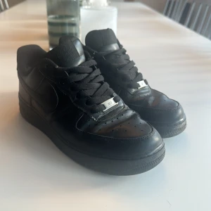 Svarta Nike Air Force sneakers - Säljer ett par klassiska svarta Nike Air Force sneakers. De är i bra skick med snygg snörning och en stilren design. Perfekta för vardagsbruk och passar till nästan allt i garderoben.