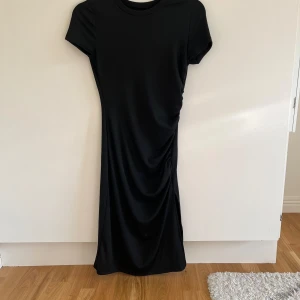 Svart långklänning - Säljer en elegant svart långklänning med korta ärmar och slits. Klänningen har en enkel och stilren design, perfekt för både vardag och fest. Materialet ser mjukt och bekvämt ut, vilket gör den idealisk för olika tillfällen.