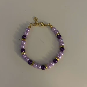 Lila pärlarmband med gulddetaljer - Snyggt armband med lila och mörklila pärlor, perfekt för att piffa upp vilken outfit som helst. Armbandet har guldfärgade detaljer mellan pärlorna och ett justerbart lås för perfekt passform. Perfekt för både vardag och fest!