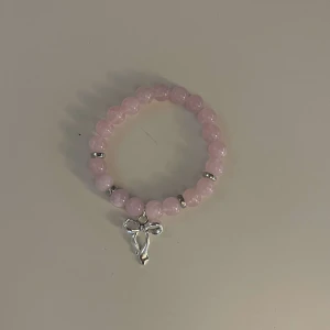 Rosa pärlarmband med silverberlock - Säljer ett supergulligt rosa pärlarmband med en fin silverberlock i form av en ängel. Armbandet är elastiskt och passar perfekt för både vardag och fest. Pärlorna är ljusrosa och ger en söt och romantisk känsla. Perfekt som present eller för att skämma bort dig själv! 💖