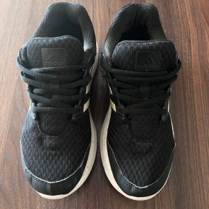 Svarta Adidas sneakers med vita detaljer - Säljer ett par svarta Adidas Cloudfoam. Mycket bekväm passform och är perfekta för både vardag och träning. Jag hade dem till träningen. Skorna är i mesh, har en vit sula och klassiska tre ränder på sidan. I mycket bra skick! Passar 37a! 😍