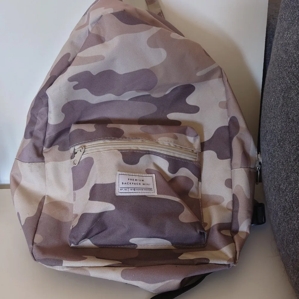 Säljer en snygg och praktisk ryggsäck i ett coolt camouflage-mönster. Den har en dragkedja framtill och justerbara axelremmar för bästa passform. Perfekt för vardagsbruk eller utflykter!. Väskor.