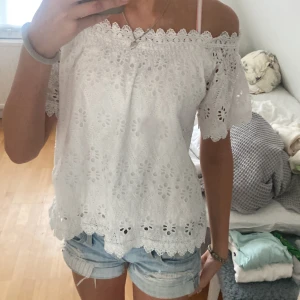 Vit off-shoulder topp från Lindex + By Malina - Säljer en superfin vit off-shoulder topp från Lindex + By Malina. Den har ett vackert broderat mönster och spetsdetaljer längs kanterna. Perfekt för sommardagar. 