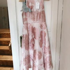 Ljusrosa blommig klänning - Ted Baker oanvänd ljusrosa klänning med blommigt mönster. Den är ärmlös och har en elegant passform som passar perfekt för sommarens fester. Materialet känns lätt och luftigt, vilket gör den idealisk för varma dagar. Perfekt för både student och midsommar! Köptes för 161 euros säljs nu för 800 kr