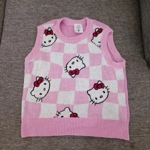 Rosa stickad Hello Kitty väst - Supergullig rosa stickad väst med Hello Kitty-motiv från Sanrio. Västen har ett rutigt mönster i rosa och vitt med flera Hello Kitty 🩷🤍 Obs betalning sker via swish 