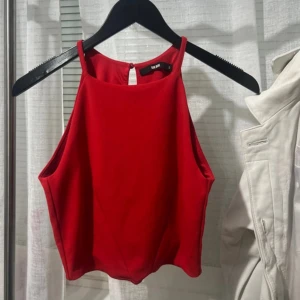 Röd ärmlös topp  - Snygg röd ärmlös topp från BikBok med hög hals och knappdetalj i nacken. Perfekt för en stilren look. Toppen är i ett mjukt material och har en figurnära passform.