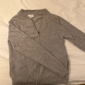 Grå kashmir från Davida. - Säljer en stilren grå tröja från davida med dragkedja framtill. Perfekt för kyligare dagar och enkel att matcha med olika outfits. Tröjan har långa ärmar och en mjuk känsla. Tröjan är gjord av 100% Kashmir.