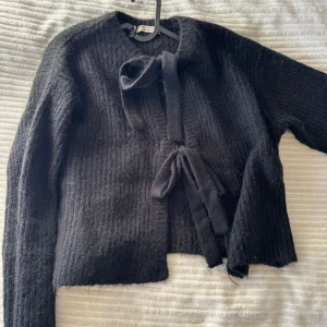 Svart stickad kofta från Gina Tricot - Mysig svart stickad kofta från Gina Tricot med knytband framtill. Perfekt för kyliga dagar med sin mjuka och varma känsla. Koftan har långa ärmar och en enkel design som passar till det mesta. Ett måste i garderoben för alla som älskar stil och komfort.