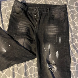 Svarta jeans med slitningar - Coola svarta jeans med slitningar och färgstänk för en edgy look. De har en klassisk femficksdesign och dragkedja. Perfekta för en avslappnad stil med en twist. Skick: 9/10.   |      W32 L32