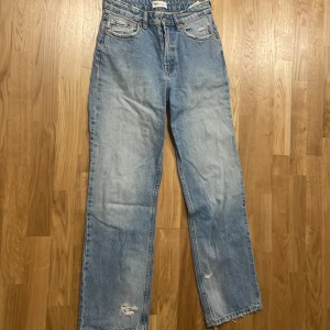 Blå jeans med slitningar på back sidan - Dessa blåa jeans med slitningar på baksidan är jättefina och sitter bra på kroppen. De är loose fit och jag har bara använt dem två gånger, så de är nästan nya. De passar verkligen till nästan allt, men är extra snygga ihop med en hoodie.