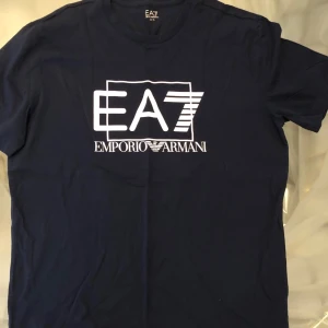 Mörkblå t-shirt från Emporio Armani - Snygg mörkblå t-shirt från Emporio Armani med det ikoniska EA7-logotypen tryckt i vitt på framsidan. Perfekt för en stilren och avslappnad look.