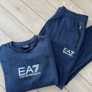 Mörkblå sweatshirt från Emporio Armani - Snygg mörkblå sweatshirt från Emporio Armani med EA7-logga på bröstet. Tröjan har långa ärmar och elastiska muddar med logotypdetaljer. Perfekt för en stilren och bekväm look.