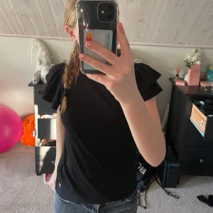 Svart blus från Pernilla Wahlgren - Snygg svart blus från Pernilla Wahlgren med korta puffärmar och subtilt randig. Blusen har en liten gulddetalj vid fållen. Jättesöt topp som passar till allt. Andvänd fåtal gånger. Pris går att diskutera💕