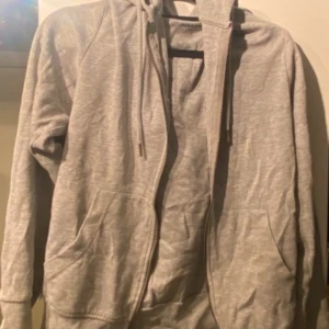 Grå hoodie från Jack & Jones - Säljer en stilren grå hoodie från Jack & Jones Essentials. Den har en dragkedja framtill och praktiska fickor. Perfekt för en avslappnad look. Passar bra till både jeans och joggers.