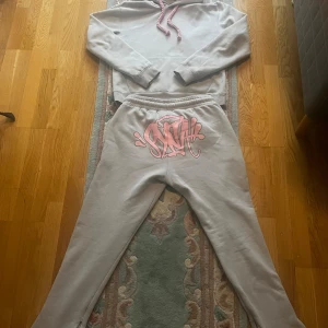 Grå hoodie och byxor med rosa detaljer - Säljer en grå hoodie och matchande byxor med rosa snören och tryck. Hoodien har en klassisk design med justerbar huva och långa ärmar. Byxorna har elastisk midja och ett coolt rosa tryck framtill. Perfekt för en avslappnad stil. pris kan diskuteras!!!