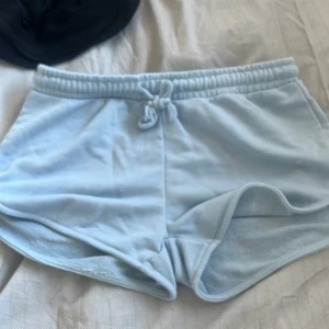 Ljusblå shorts med snörning - Säljer ett par ljusblå shorts med elastisk midja och snörning. Perfekta för en avslappnad stil under varma dagar. De är mjuka och bekväma, vilket gör dem idealiska för både hemmamys och utomhusaktiviteter.