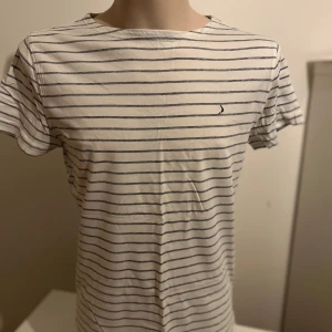 Vit och blå randig t-shirt från Boomerang - Säljer en klassisk vit t-shirt med blå ränder från Boomerang. Den har en liten broderad logga på bröstet och är kortärmad. Perfekt för en avslappnad stil.