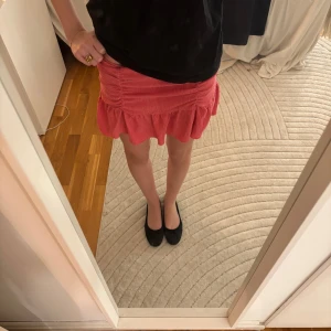 Rosa kjol med volang - Säljer en snygg röd kortkjol med volangdetaljer. Kjolen har en åtsittande passform och är perfekt för att ge en färgklick till din outfit. Den är gjord i ett mjukt och bekvämt material.