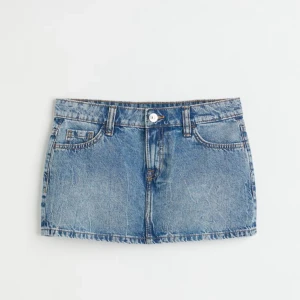 Lågmidjad jeanskjol från Angelic - En kort 5-fickskjol i vävd bomullskvalitet. Kjolen har låg midja och bakfickor med lock och knapp. Gylf med dragkedja och knapp. Midja 38cm rakt över 