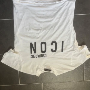 Vit t-shirt från Dsquared2 - Säljer en vit t-shirt från Dsquared2 med texten 'ICON' tryckt i svart på framsidan. T-shirten är kortärmad och har en klassisk rund halsringning. Perfekt för en stilren och modern look.