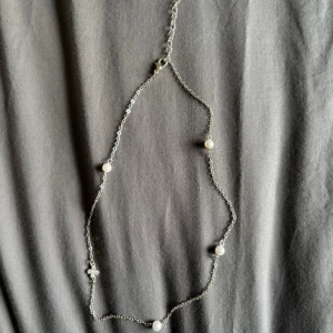 Silverfärgat halsband med pärlor - Elegant silverfärgat halsband med små vita pärlor jämnt fördelade längs kedjan. Perfekt för att ge en stilren touch till din outfit. Justerbar längd för bästa passform. EJ ÄKTA!