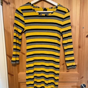 Randig gul och svart klänning från Gina Tricot - Säljer en cool randig klänning i gult och svart med långa ärmar. Den har en ribbad struktur och en bekväm passform som passar perfekt för både vardag och speciella tillfällen. Perfekt för dig som vill sticka ut!