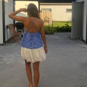 Blå blommig linnetopp - Säljer en söt blå linnetopp med vita blommor. Köpt i Frankrike från märket Etam! Toppen har smala axelband som korsas i ryggen och en luftig passform. Perfekt för varma sommardagar!