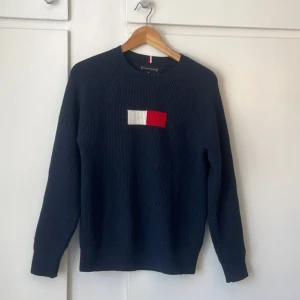 Marinblå stickad tröja från Tommy Hilfiger - Snygg marinblå stickad tröja från Tommy Hilfiger med deras logotyp i rött och vitt på bröstet. Tröjan är väldigt mysig och skön! Använd fåtal gånger 🩷