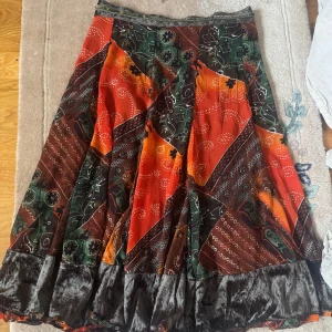 Färgglad långkjol från You and Me - Säljer en färgglad långkjol från You and Me med ett unikt mönster i rött, grönt och orange. Kjolen har ett blommigt mönster och är perfekt för att ge en bohemisk touch till din stil. Den är tillverkad i ett mjukt material som ger ett fint fall. Perfekt att ha utomlands eller som en statment peice. Skulle gissa på en s.