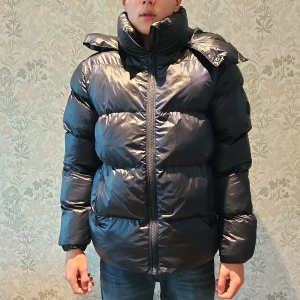 Mörkblå pufferjacka från Everest - Säljer en snygg svart pufferjacka från Everest. Jackan har en hög krage och en justerbar huva för extra skydd mot kyla. Den är långärmad och har en dragkedja framtill. Perfekt för kalla dagar! Är 178cm och den sitter perfekt. 