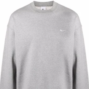 Grå tröja från Nike - Säljer en klassisk grå sweatshirt från Nike med rund hals och en liten vit logga på bröstet. Perfekt för en avslappnad stil. Passar bra till både jeans och träningsbyxor.