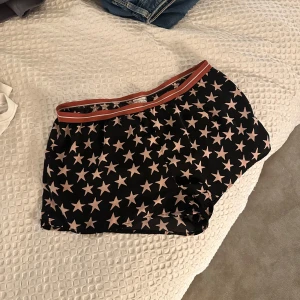 Love stories Svarta shorts med stjärnmönster  - Snygga svarta shorts från Love stories x H&M med ett coolt stjärnmönster i rosa. De har en elastisk midja med en röd randig detalj. Perfekta för en avslappnad stil.
