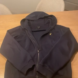 Mörkblå hoodie från Lyle & Scott - Säljer en snygg mörkblå hoodie från Lyle & Scott med dragkedja, storleken 15-16 men skulle säga storlek S, finns tecken på användning 