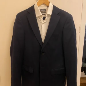 Kostym (Kavaj,Skjorta,Byxor) Dresmann  - Kostym i slim fit från Dressmann i mycket bra skick säljes. Passar dig som är ganska långsmal. Inköpt 2023 för ca 2000 kr. Ingår kavaj 46 Long, Skjorta 37/38 small extra long, Byxor 29/32. Slänger med en fluga också. Hör av dig om du vill ha fler bilder. Postar Asap efter köp.