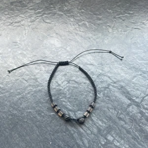 Svart armband med justerbar knytning - Snyggt svart armband med justerbar knytning och små fyrkantiga pärlor. Perfekt för en stilren look och passar till alla tillfällen. Armbandet har en enkel design med en mix av runda och fyrkantiga pärlor.