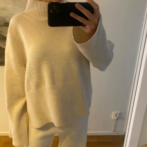 Beige stickad polotröja - Säljer en mysig beige stickad polotröja med ribbade detaljer. Tröjan har långa ärmar och en hög krage som håller dig varm under kyliga dagar. Perfekt för en stilren och bekväm look.