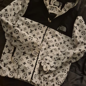 Mönstrad jacka från The North Face - Säljer en unik jacka från The North Face med ett iögonfallande mönster i svart och vitt. Jackan har dragkedja och en huva, perfekt för att sticka ut i mängden. Den är långärmad och har elastiska muddar vid ärmslut och nederkant.