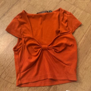 Orange ribbad topp med rosett - Säljer en snygg orange ribbad topp med korta ärmar och en söt rosett framtill. Köpt på veromoda.