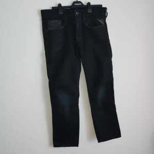 Svarta jeans från Replay - Snygga svarta jeans från Replay med klassisk femficksdesign och knappgylf. De har en stilren look och passar perfekt för en avslappnad stil. Märkeslappen i brunt läder ger en extra touch av kvalitet.