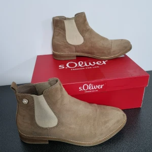 Bruna Chelsea boots från s.Oliver - Snygga bruna Chelsea boots från s.Oliver i mocka med elastiska paneler i beige. Perfekta för en stilren look och enkla att ta på och av. Passar utmärkt till både jeans och klänning.