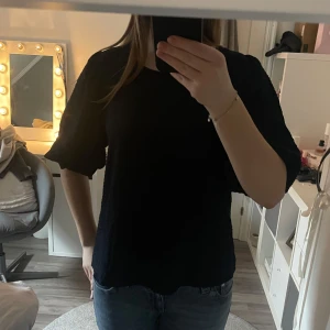 Mörkblå blus med puffärmar - Mörkblå blus från JDY med puffiga trekvartsärmar och en rund halsringning. Blusen har en texturerad yta och en knappdetalj i nacken.