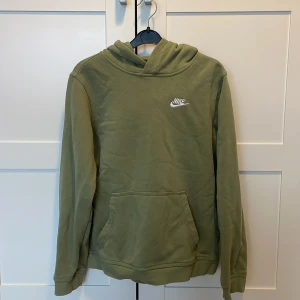 Olivgrön hoodie från Nike - Säljer en olivgrön hoodie från Nike med broderad logga på bröstet. Tröjan har en klassisk känguruficka och långa ärmar. Perfekt för en avslappnad stil. 🧥Nypris 500kr!