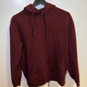 Vinröd hoodie - Säljer en vinröd hoodie med en klassisk design. Den har en stor ficka framtill och justerbar huva med dragsko. Perfekt för en avslappnad stil. 100% bomull.