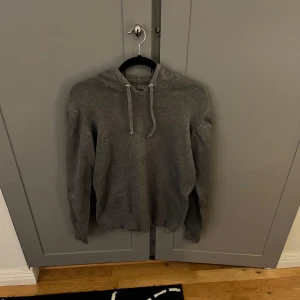 Grå hoodie - Säljer en stilren stickad grå hoodie med justerbar huva och ribbade muddar.  