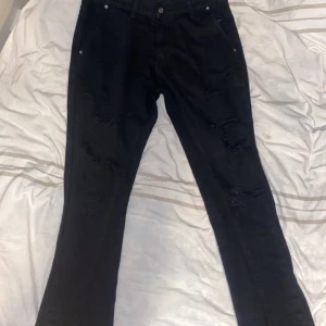 Svarta jeansbyxor - Snygga svarta jeansbyxor med klassisk design. De har en rak passform och är perfekta för en stilren look. Byxorna har knappar och dragkedja framtill.