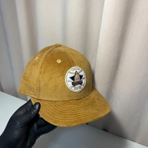 New Era keps - Snygg brun keps i manchester från New Era med broderad logga framtill. Perfekt för en avslappnad stil. Kepsen har en klassisk passform och är en del av 59FIFTY-kollektionen.
