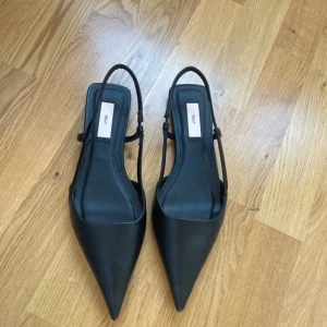 Svarta pumps från Nelly - Eleganta svarta pumps från Nelly med spetsig tå och smala remmar. Perfekta för en stilren look. Har aldrig använts. 