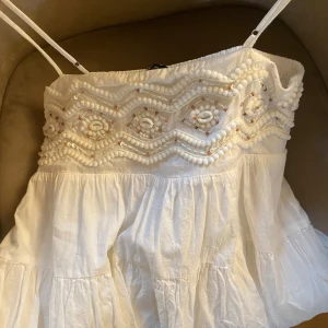 Vit puffig klänning från Zara - Säljer en söt vit klänning från Zara med axelband och vackra snäckor broderade på överdelen. Perfekt för varma dagar med sin lätta och luftiga design. Köpt i sommras och använd fåtal gånger sedan i Spanien 🌺sååå snyggg verkligen, säljer för att den har blivit för liten💔
