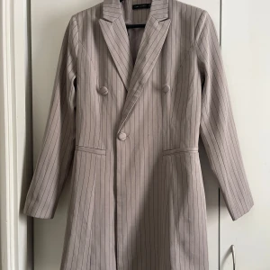 Kavaj från ISAWITFIRST - Kavajen har lång ärm med inga fickor och kan användas som en klänning. Perfekt för en stilren look. 